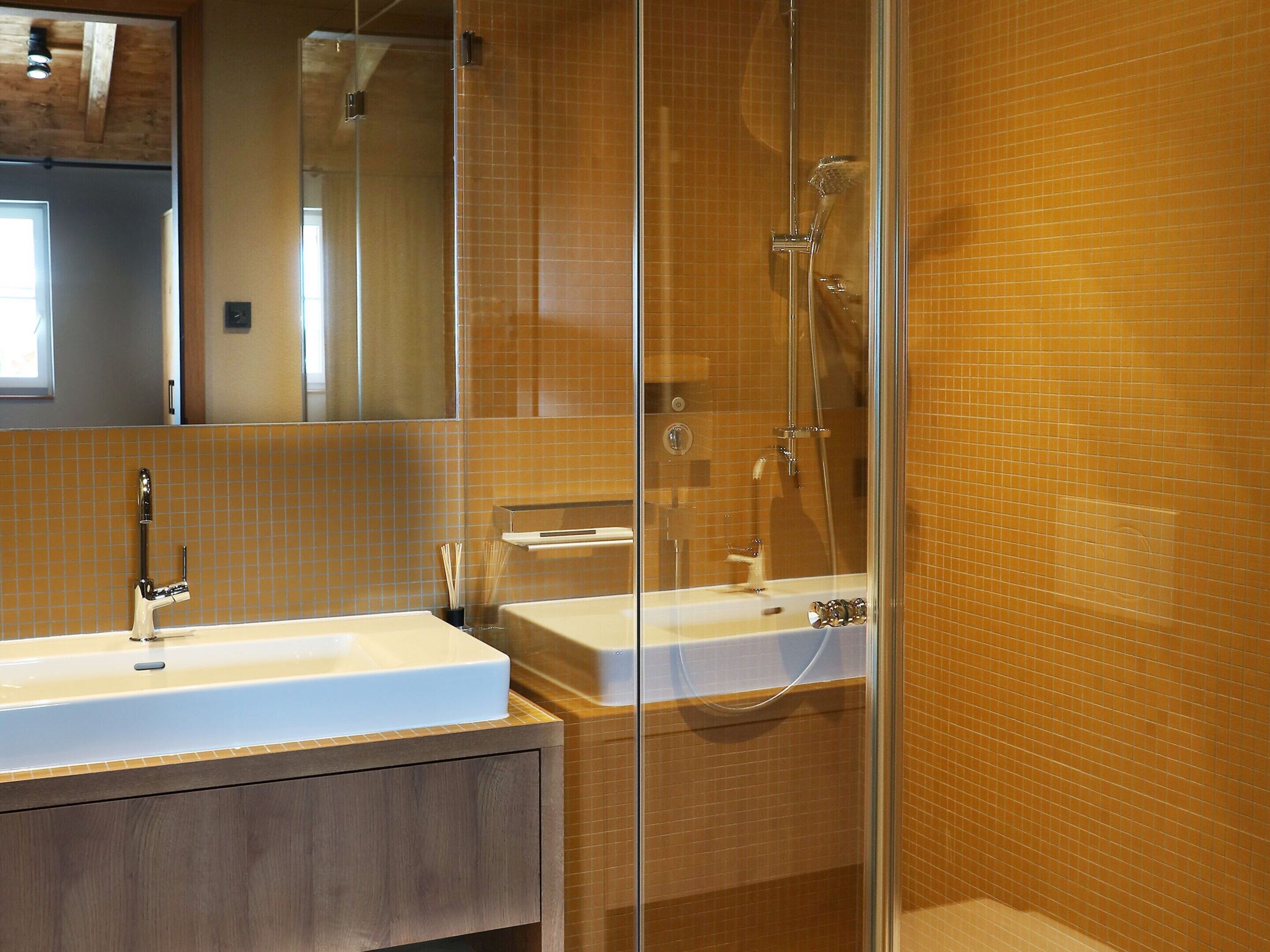 Un baño moderno con cabina de ducha de vidrio, tocador de madera y pared con azulejos.
