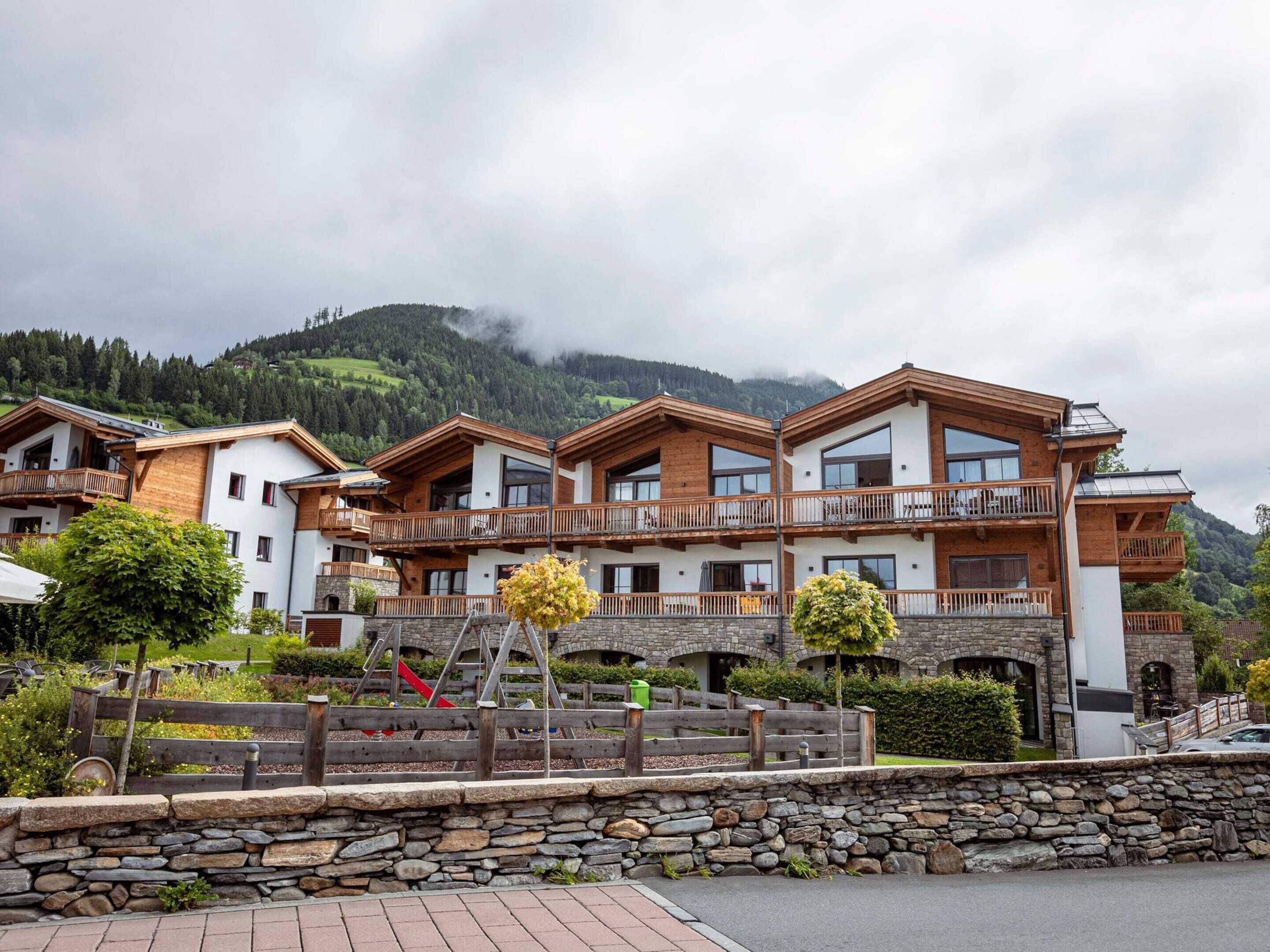 Un hotel de varios pisos con balcones de madera y paredes de piedra, con montañas al fondo.