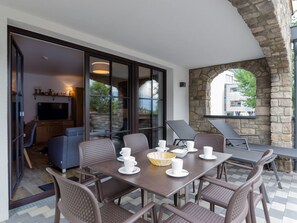 A dining area with a table set for four, surrounded by wicker chairs, and a stone archway leading to an outdoor seating area.