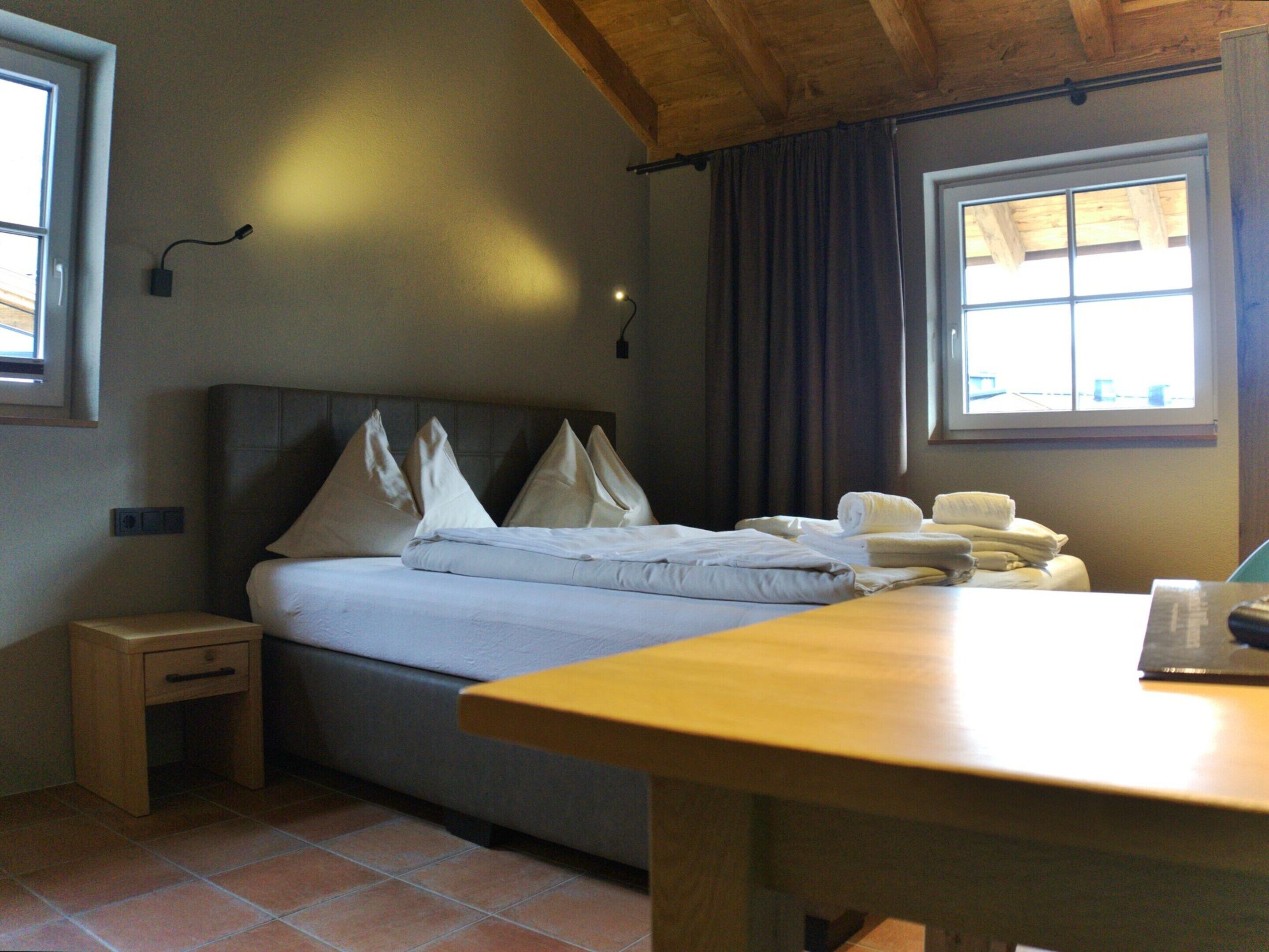 A neatly made bed with pillows, a bedside table, and a window with curtains.