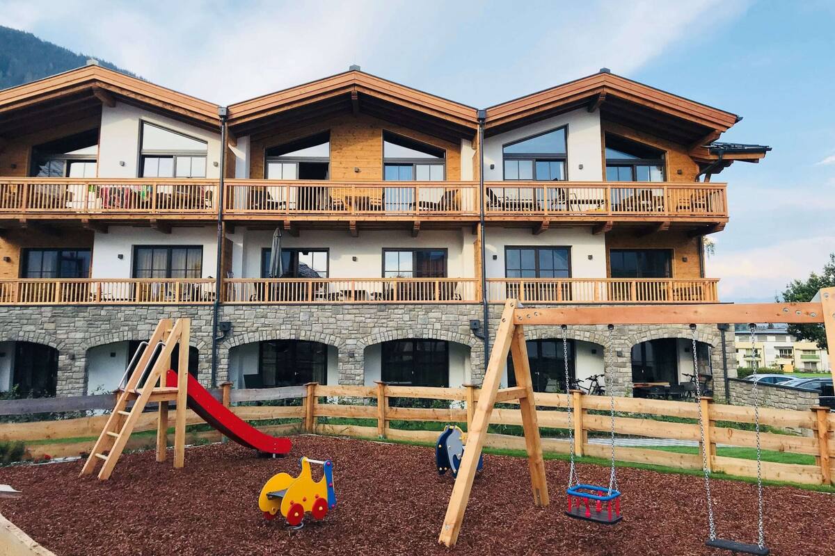 A multi-story building with balconies, a playground with a slide, and a stone facade.