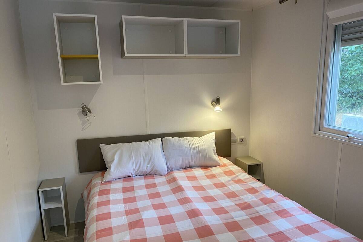 Un dormitorio con una colcha a cuadros, dos mesitas de noche y estanterías en la pared.