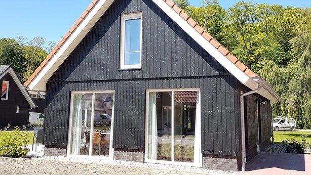 A modern two-story building with a dark facade, white trim, and a red-tiled roof. It features large glass doors and windows, providing ample natural light. - Cozy House With a Dishwasher in the Middle of the Achterhoek (Almen)
