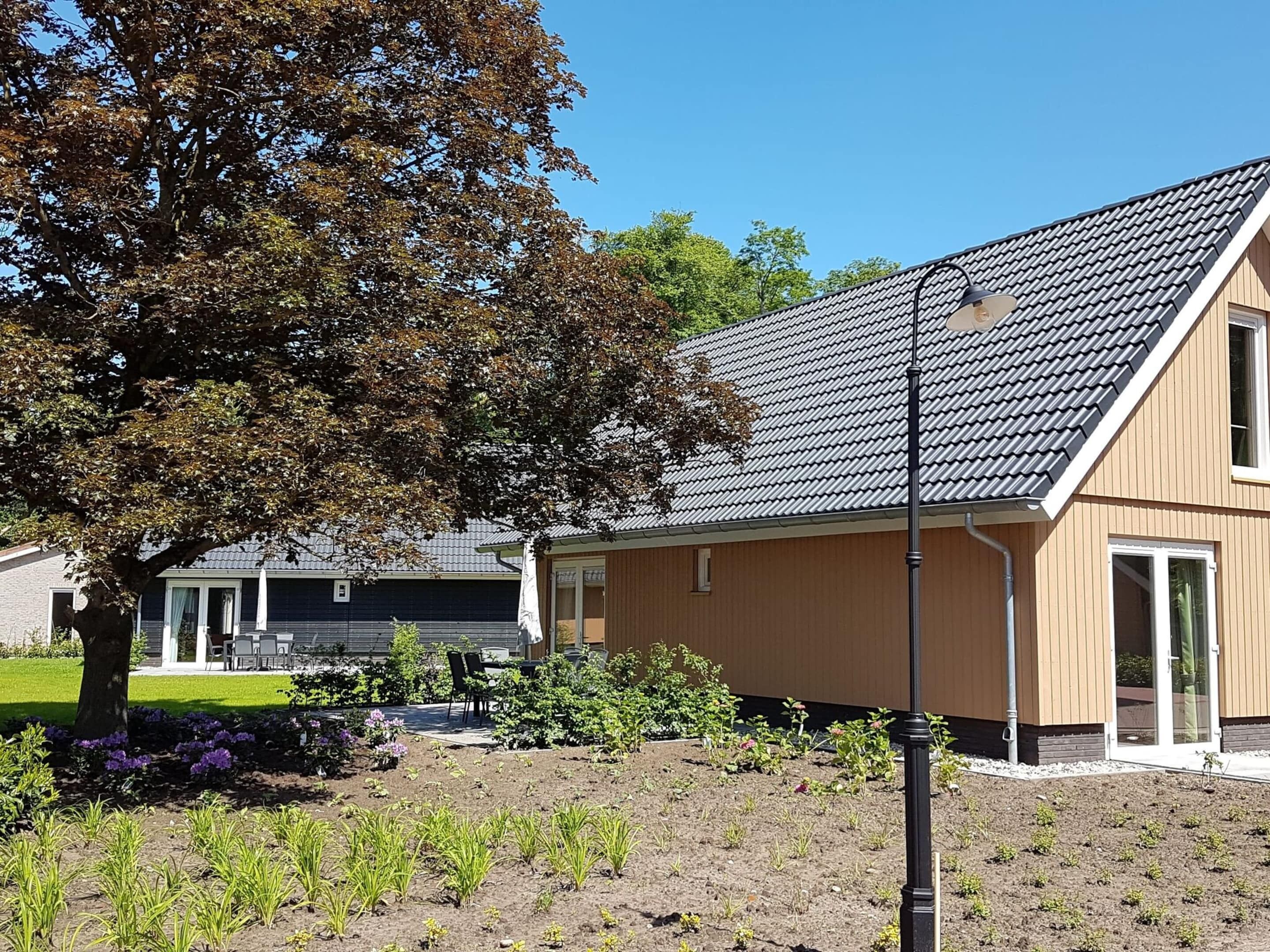 Ein Wohngebäude mit Satteldach, ein Garten mit jungen Pflanzen und ein Baum im Vordergrund.