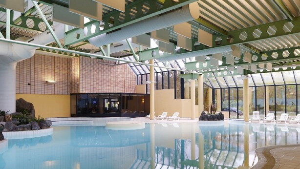 An indoor swimming pool with clear water, surrounded by lounge chairs and a modern architectural design with green structural elements and large windows. - Modern Suite With Combi-microwave, Close to Durbuy (Durbuy)