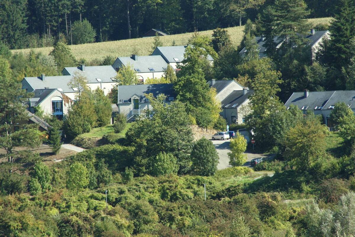 A cluster of houses with sloped roofs, surrounded by dense greenery and trees.