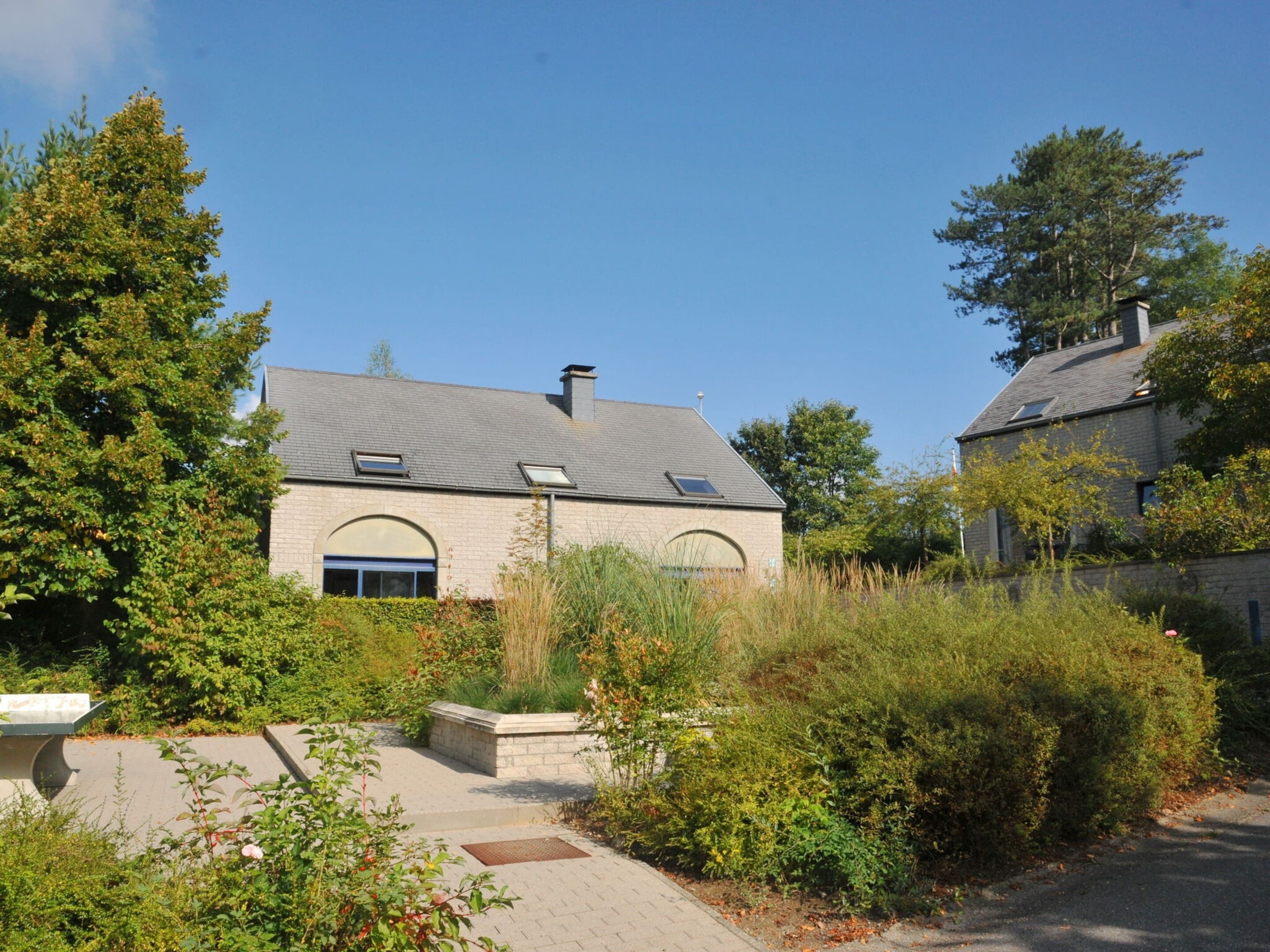 A two-story house with a stone facade, a sloped roof, and a small garden area with a bench.