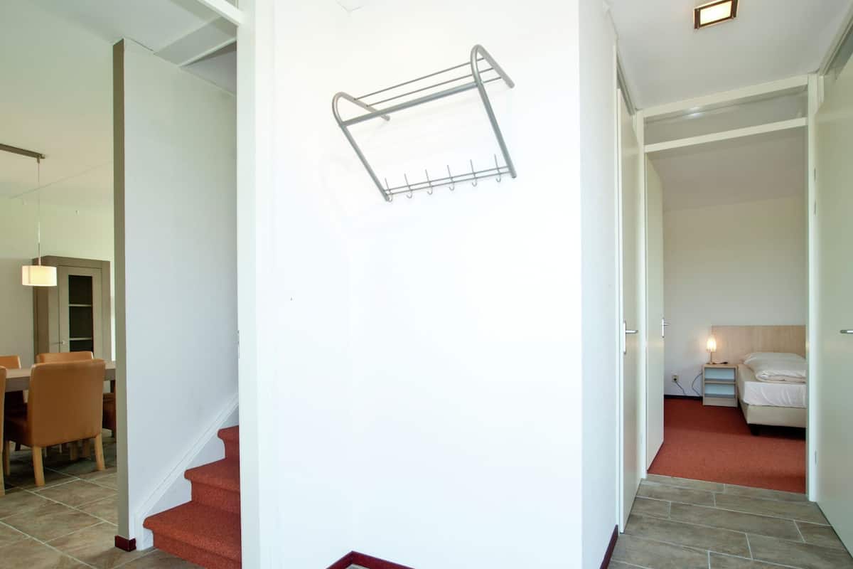 Un intérieur moderne avec un escalier menant à une salle à manger, une chambre avec un lit et une table de chevet, et un étendoir fixé au mur.