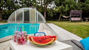 Ein Poolbereich mit einem Glastisch, auf dem eine Wassermelifeilschenke und Einmachgläser mit Strohhalmen stehen.