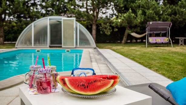 Escena junto a la piscina con una mesa de vidrio que sostiene una rebanada de sandía y frascos con pajitas.