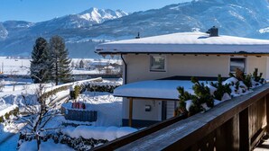 Une maison de montagne enneigée, dotée d’une terrasse en bois et offrant une vue sur les montagnes.