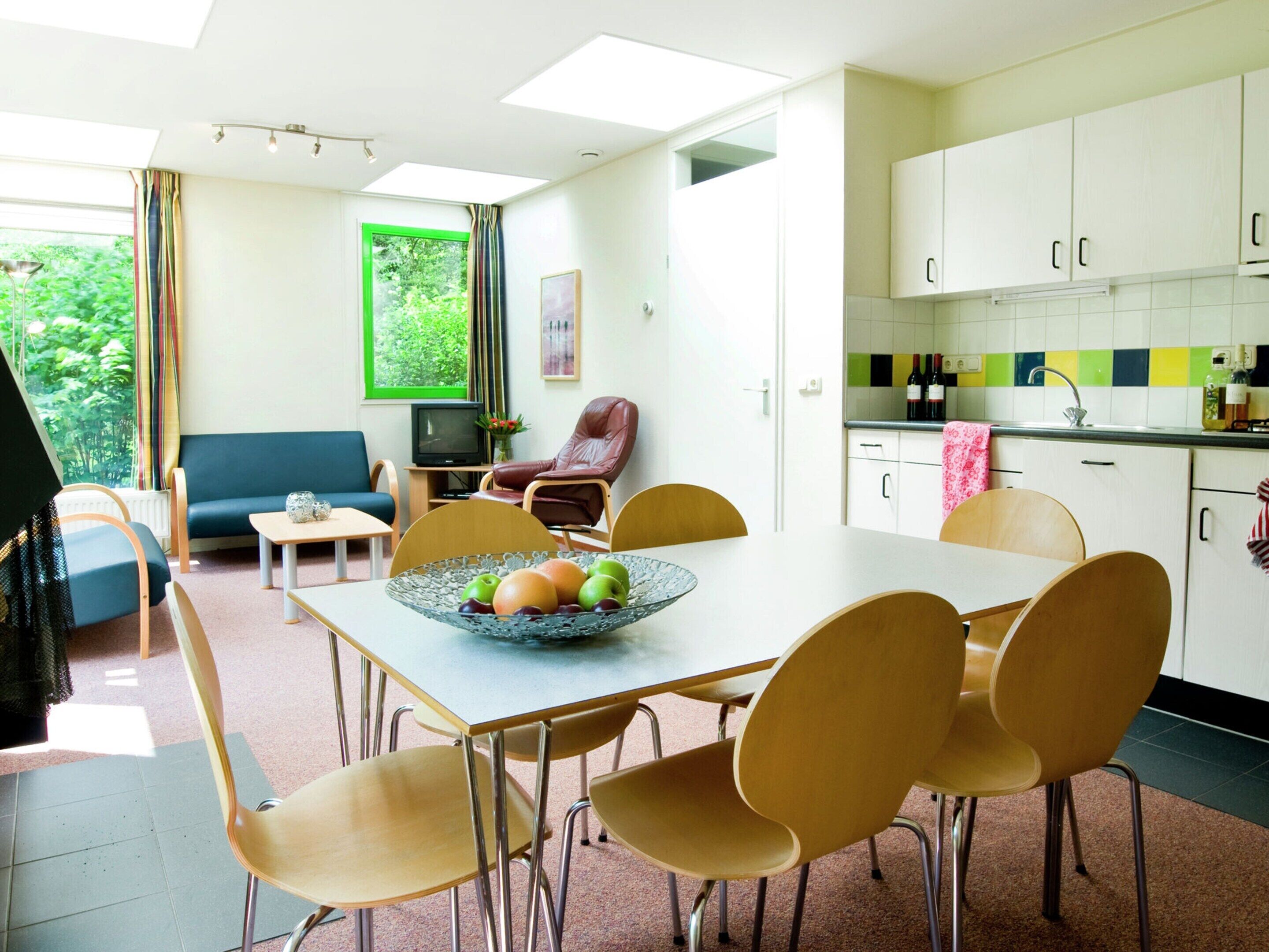 Una cocina moderna con armarios blancos, una mesa de comedor con sillas, un televisor y una ventana con cortinas.