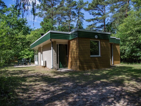 A small cabin with a green roof and a single window, surrounded by trees.
