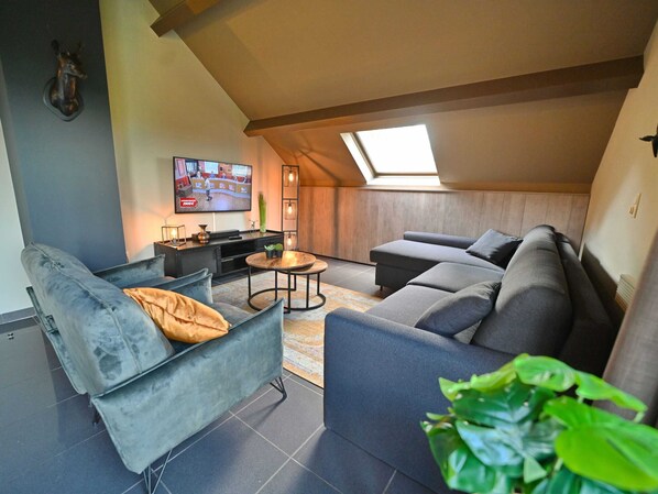 Un salon moderne de style industriel, avec un grand canapé, un fauteuil plus petit, une table basse et un téléviseur fixé au mur.