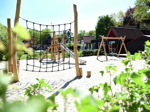 Un parque infantil con una estructura de escalada con red, un tobogán y columpios.