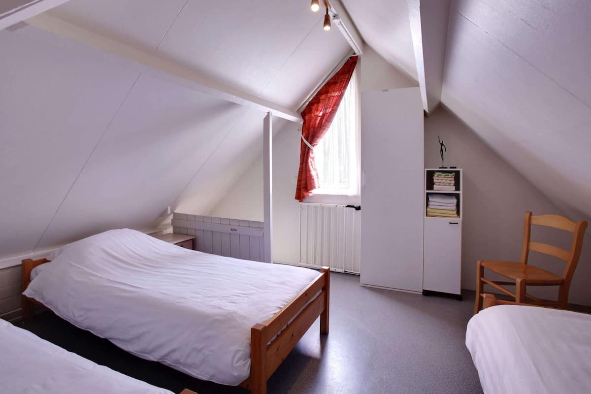 Ein Schlafsaalzimmer mit schrägen Wänden, einem hölzernen Bett, einem Stuhl und einer Heizung.