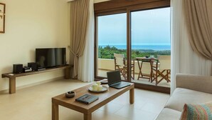 A living room with a TV, laptop, and books on a wooden table, a sofa, and a balcony with a view of the sea. - New Villa With Private Pool, Privacy, Near sea and Arkadi Monastery on NW Coast (Rethymno)