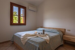 A bedroom with a bed, a bedside table, a nightstand, a window with a view, and an air conditioning unit. - Holiday Resort, Budoni (Budoni)
