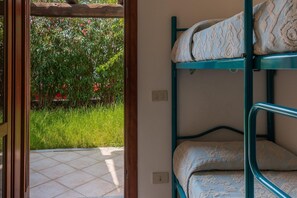 A bunk bed with patterned bedding, a tiled floor, and a view of a garden with green foliage and red flowers.