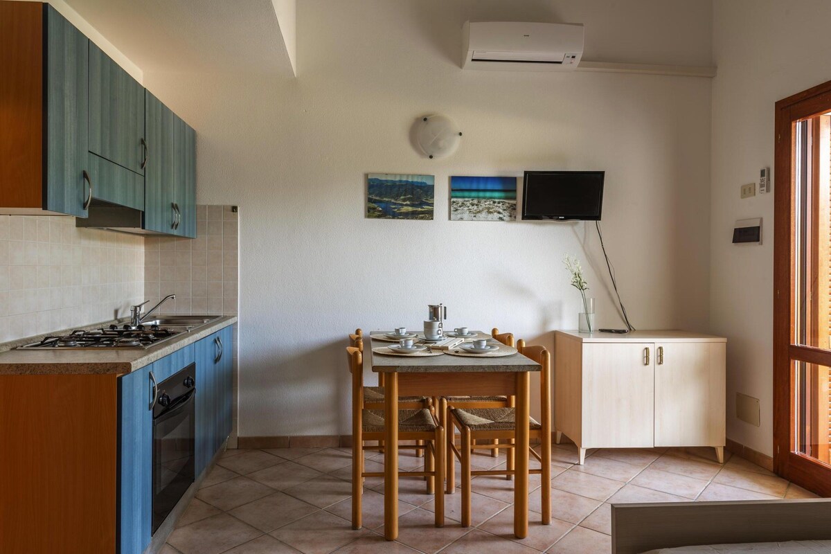 Een keuken met blauwe kastjes, een eettafel met stoelen, een fornuis en een televisie aan de muur.