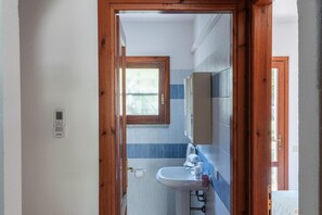 Un baño con puerta de madera, ventana, lavabo y espejo.