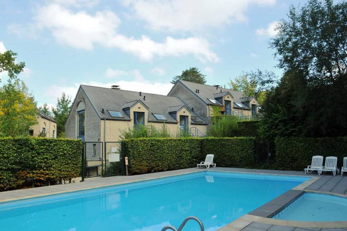 A swimming pool with a clear blue water, surrounded by a hedge and a row of white lounge chairs.