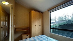 Ein kompaktes Wohnmobil-Interieur mit einem Bett, Holzschränken und einem Fenster mit Blick nach draußen.