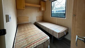 Ein kompaktes Wohnmobil-Interieur mit zwei gestreiften Betten, einem Fenster mit Blick und einem Holzkasten.