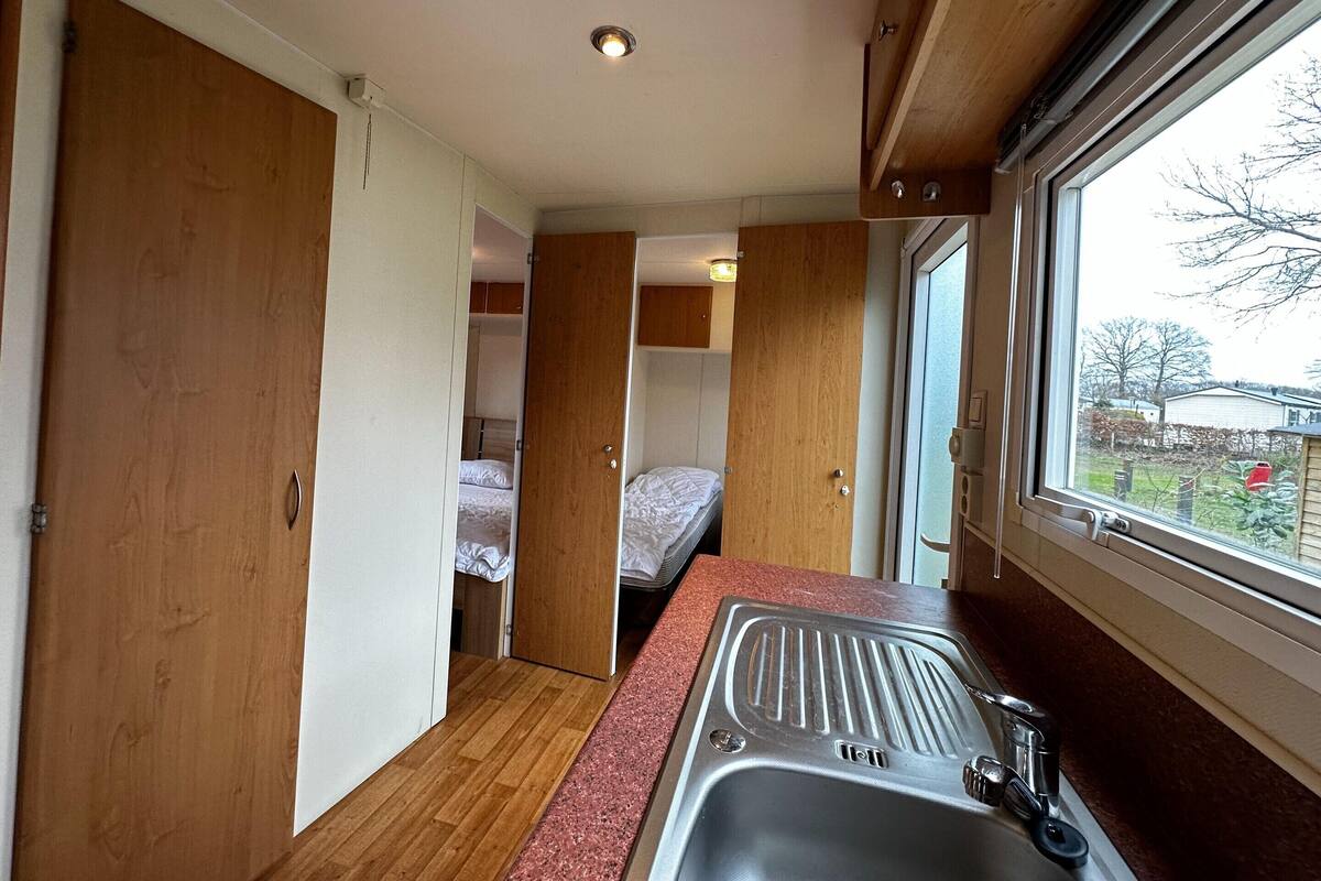 A compact kitchenette with a sink, wooden cabinets, and a window with a view of the outside.