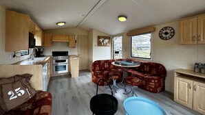 Eine kompakte Küchenzeile in einem Wohnmobil mit Holzschränken, einem Herd und einem Spülbecken. Es gibt eine kleine Essecke mit Tisch und Stühlen sowie eine Sitzecke mit einer Couch.