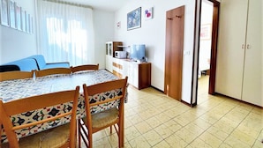 A room with a dining table, chairs, a TV, and a wardrobe. - Modern Apartment in Caorle With Private Terrace (Caorle)