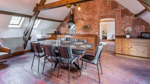 A loft-style kitchen with exposed wooden beams, a brick wall, and a dining area with a round table and chairs. - Nice Apartment on Unesco World Heritage Site Wortel-kolonie (Hoogstraten)
