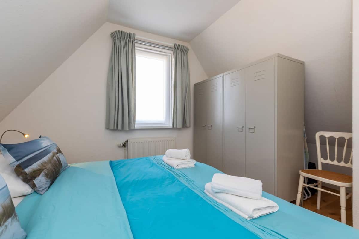 A bedroom with a bed, a wardrobe, a chair, and a window with curtains.