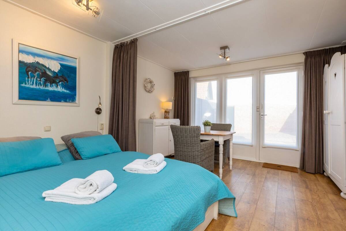 A hotel room with a bed, a desk, a chair, a small table, a window, and a door.
