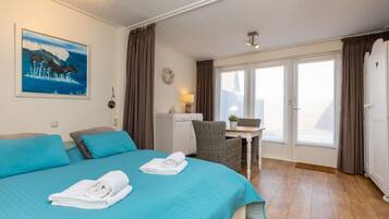 A hotel room with a bed, a desk, a chair, a small table, a window, and a door.