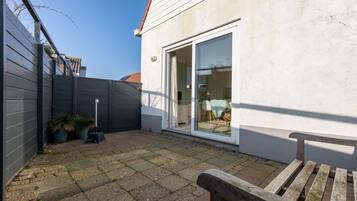 A patio with a wooden bench, a sliding glass door leading to an interior space, and a grey fence.