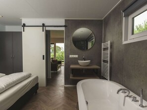 A modern bathroom with a freestanding bathtub, a round mirror, and a built-in sink. - Wellness Lodge With Sauna and Wonderful Views (Zuna)