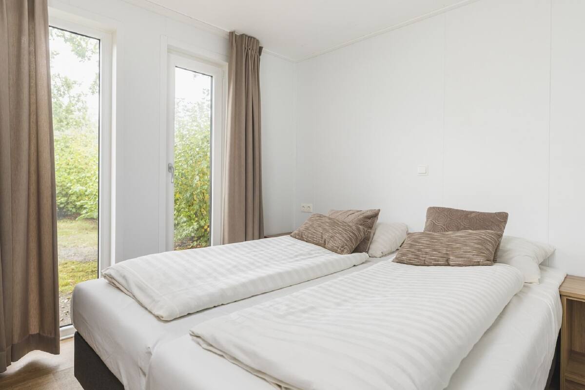 A bedroom with two beds, a window, and a view of greenery outside.
