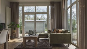 A spacious living room with a large window, a sofa, a coffee table, and a chair. - Wellness Lodge With Sauna and Wonderful Views (Zuna)