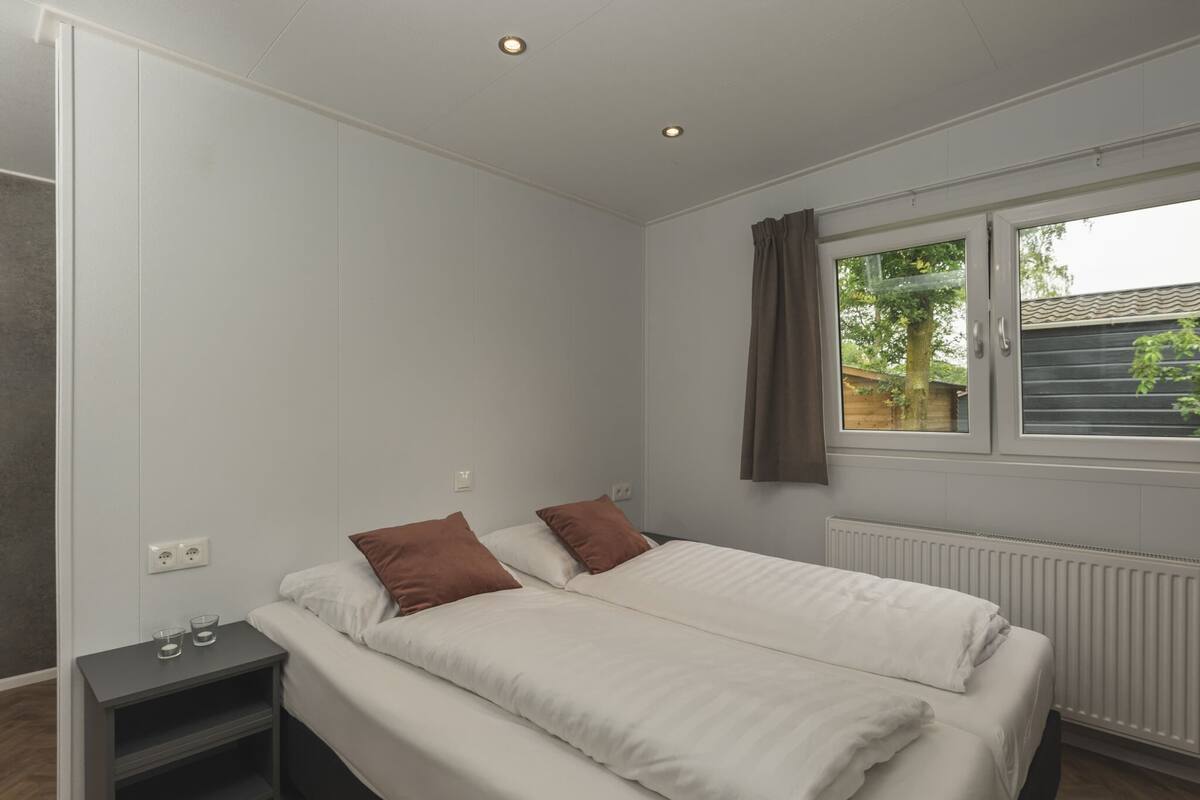 A bedroom with a bed, bedside tables, a window with curtains, and a radiator.