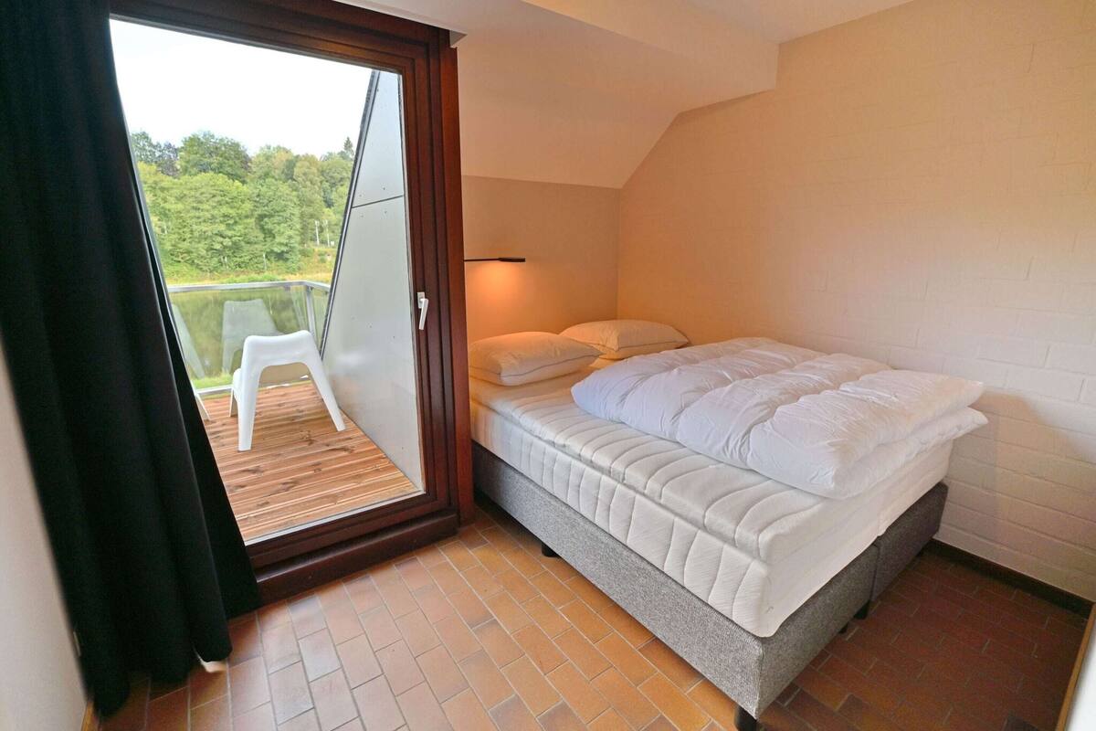 Un dormitorio con una cama, un ventanal corredizo que da a un balcón y piso de baldosas.