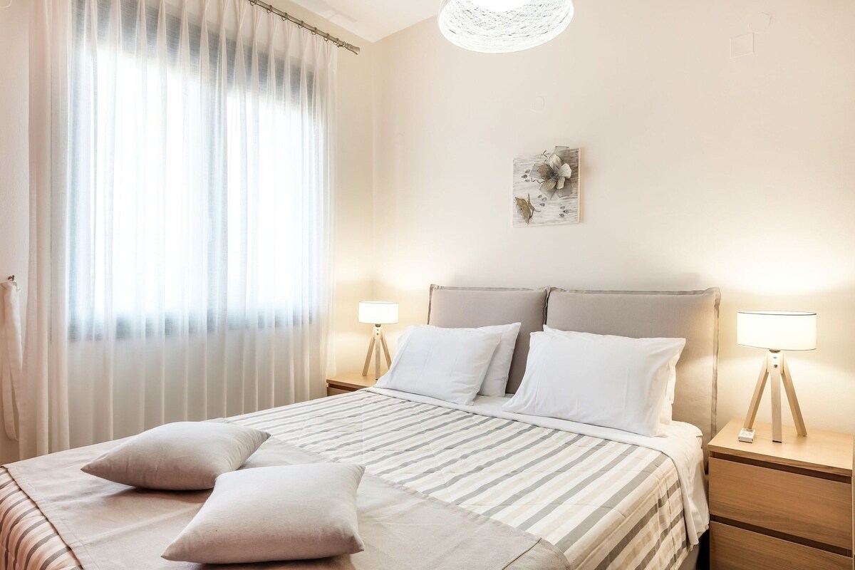 Een slaapkamer met een bed, twee nachtkastjes, een lamp en een wanddecoratie.