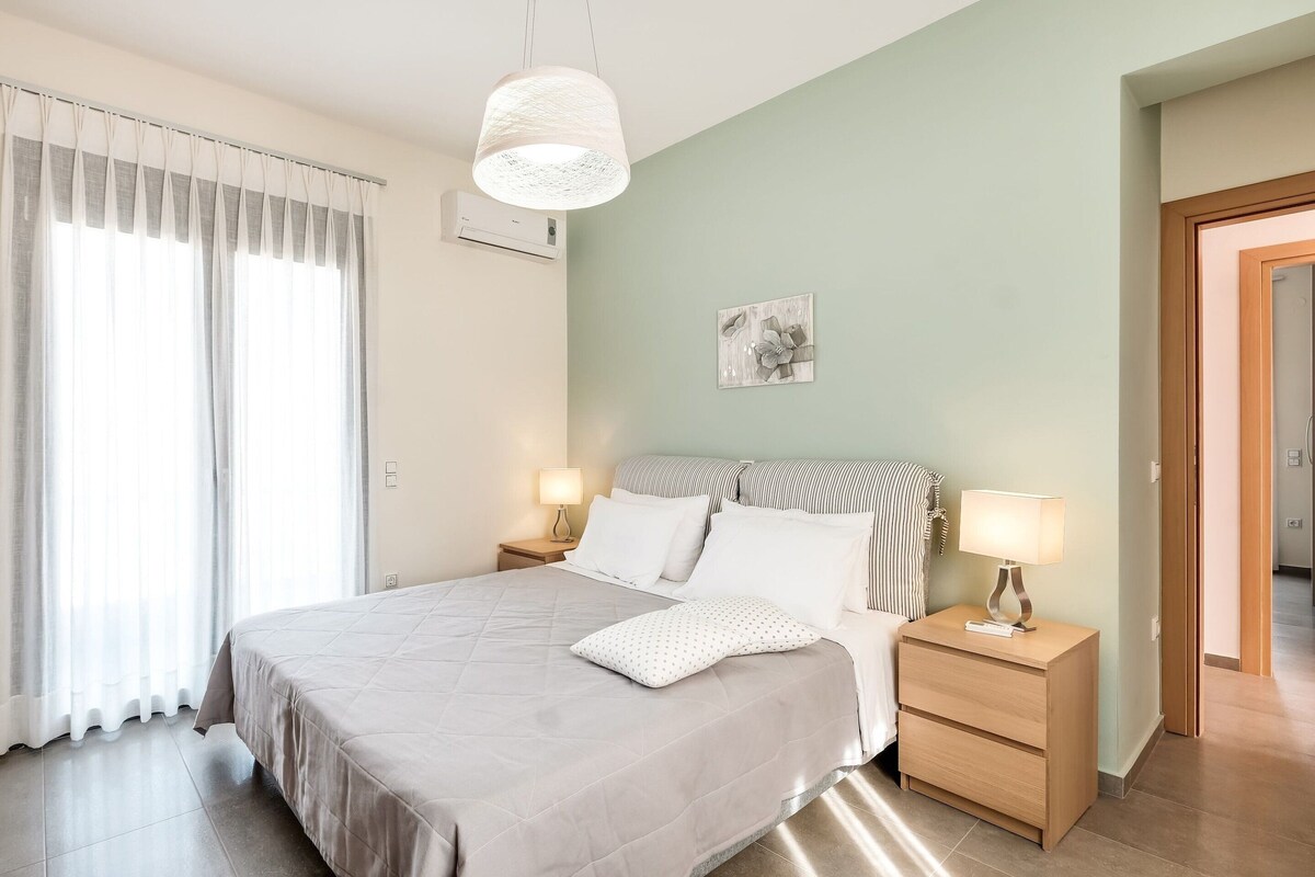 Een slaapkamer met een bed, nachtkastjes, een hanglamp en een wandairconditioner.