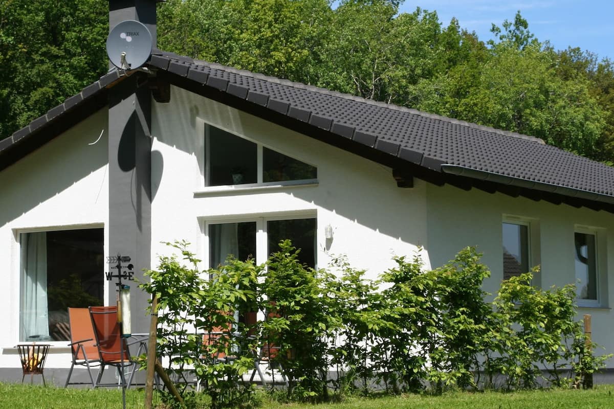 A white house with a sloped roof, a satellite dish, and a garden with chairs and plants.