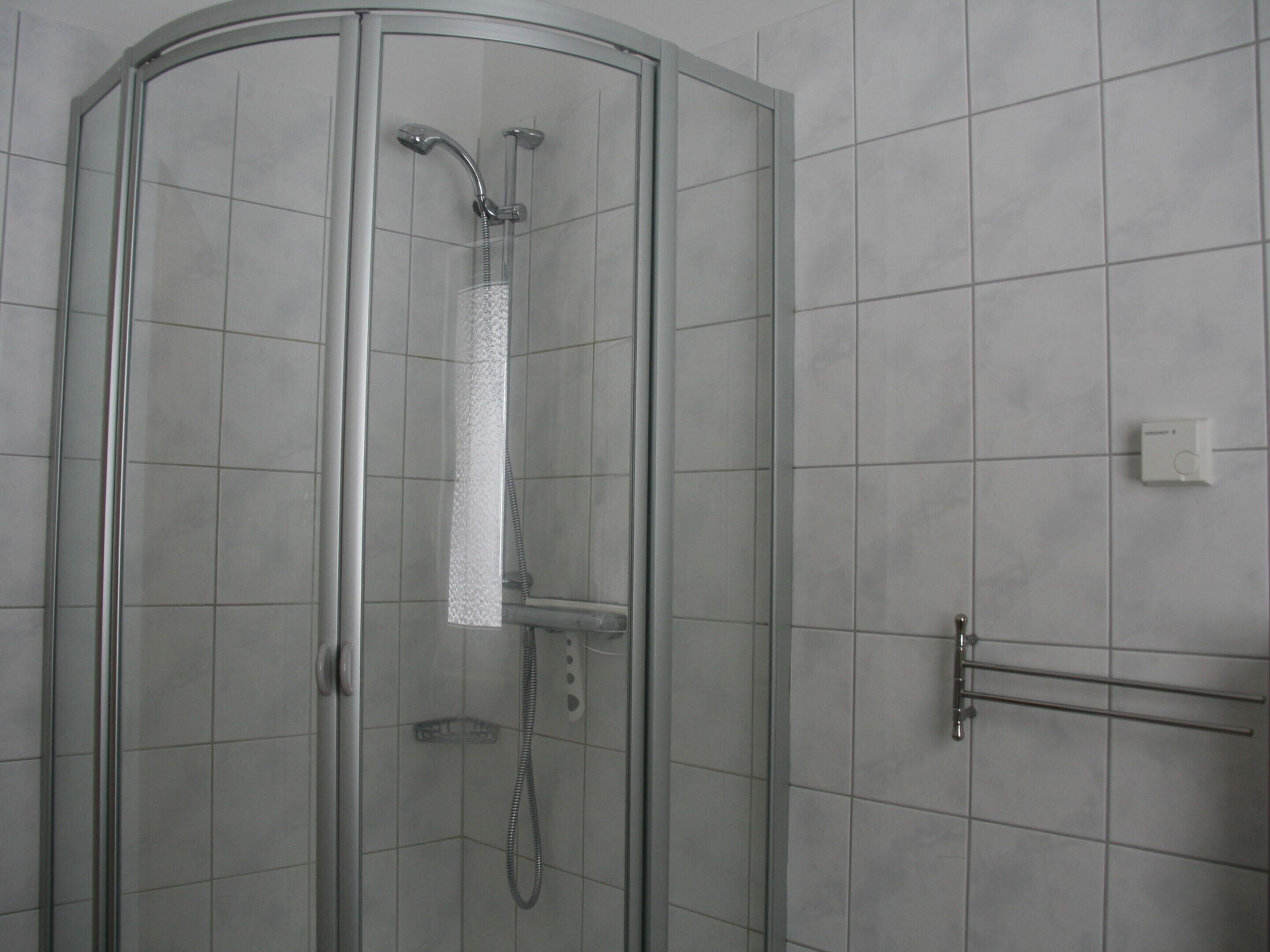 Una ducha con paredes de vidrio, un cabezal de ducha manual y un cabezal de ducha fijo en la pared.