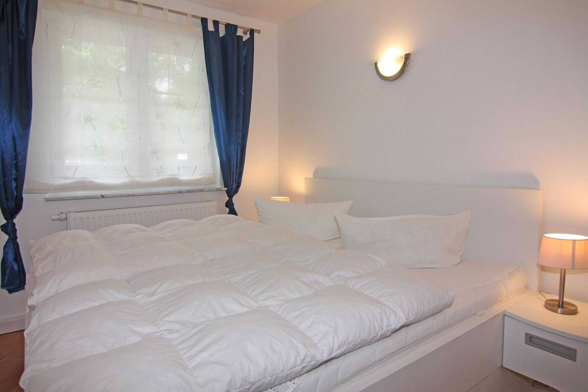A neatly made bed with white bedding, a bedside lamp, and a wall-mounted light fixture.
