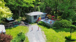 A small house with a deck, surrounded by lush greenery. - Spa & River view | Le Jardin (Montmagny)
