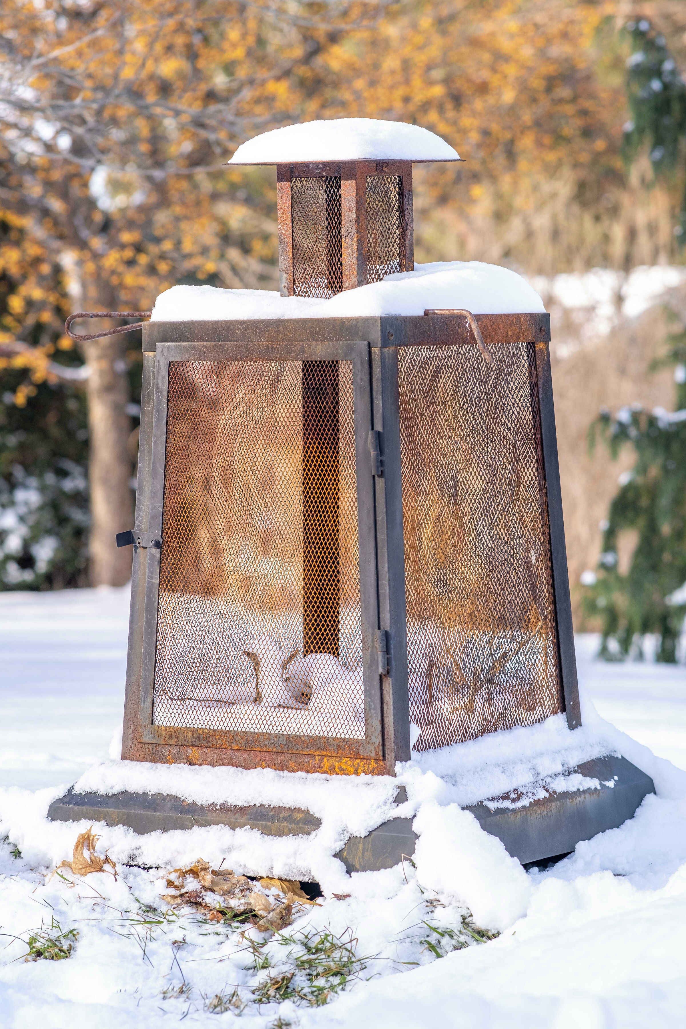 Une mangeoire à oiseaux en métal, recouverte de neige, dotée d’une structure en treillis et dont le sommet est également enneigé.