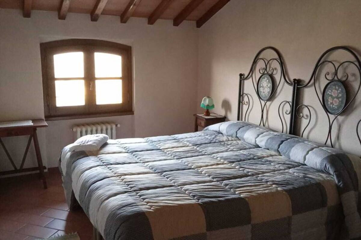 A bedroom with a bed, a window, a radiator, a desk, and a lamp.
