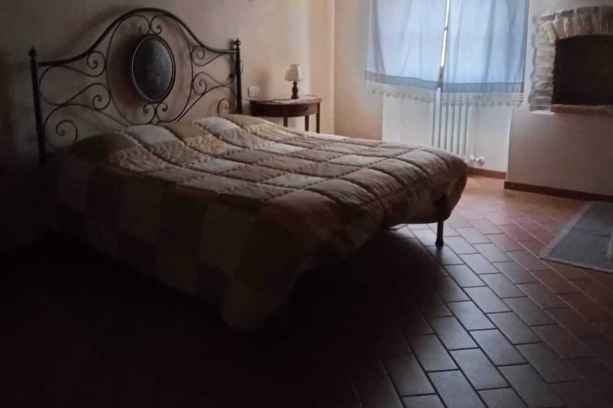 A bedroom with a bed, a nightstand, a window with curtains, and a fireplace.